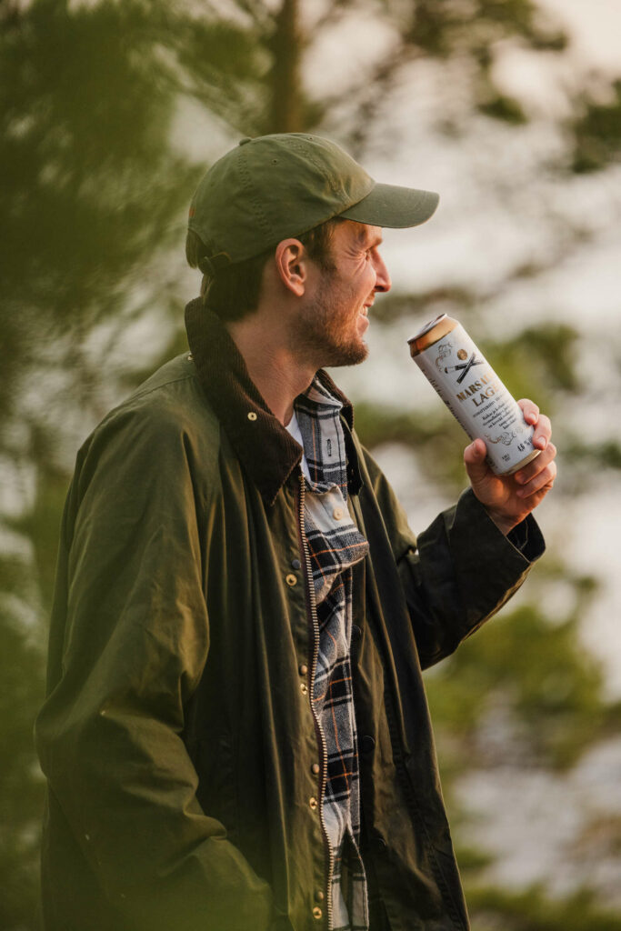 Mies, jolla vihreä takki ja lippis juo Marsalkka lageria oluttölkistä