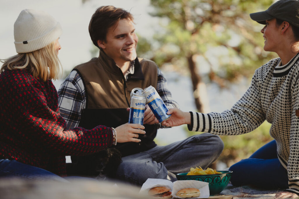 Kaksi naista ja yksi mies eväsretkellä kalliolla järven ääressä.